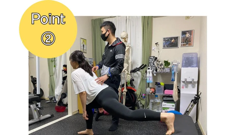 トレーナーがフォームを確認しながら、利用者がランジ姿勢でストレッチしている様子(Point②)